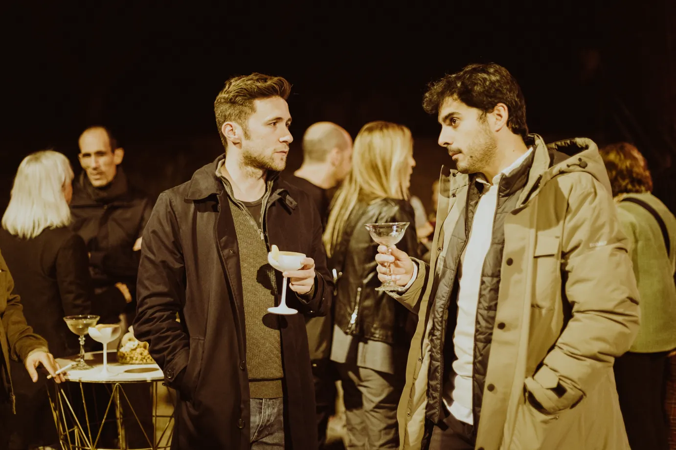 Invitados conversando con copas en evento nocturno